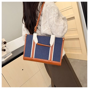 Detail showing blue denim fabric and brown leather stitching on a large tote bag