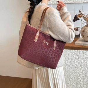 Deep red leopard print tote bag with golden bow ornament shown on a model