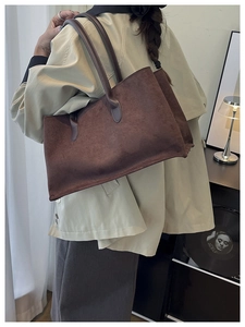 Detail of a large brown suede tote bag carried by a model in a modern home setting