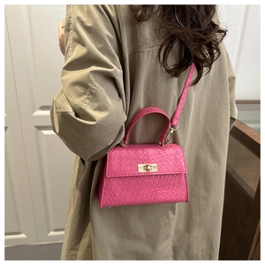 Sac bandoulière fuchsia à motif tissé et fermoir doré porté sur un trench-coat kaki