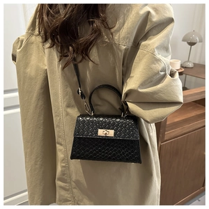 Détail d'un sac à main noir motif crocodile avec fermoir doré porté sur un trench