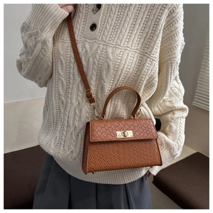 Brown croc-embossed square crossbody bag worn over a beige knit sweater on a model