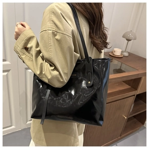 Detail of glossy black patent leather tote bag with metal brand tag worn over the shoulder