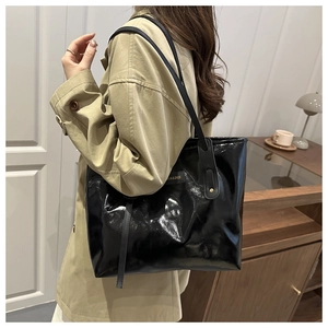 Detail of glossy black tote bag with gold fashion label and slim shoulder straps