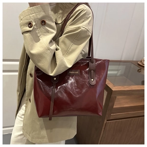 Detail of burgundy patent leather tote bag with gold buckles on khaki trench coat