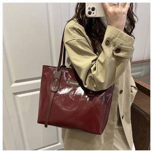 Detail of burgundy glossy tote bag with gold metal logo plate and brown leather straps