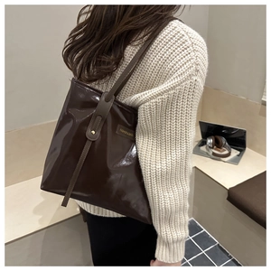 Detail of dark brown glossy tote bag with metal tag shown on a knitted sweater