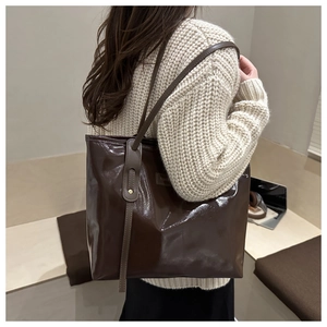 Detail of glossy dark brown tote bag with metal rivets and FASHION label on shoulder strap