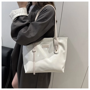 Close-up of white patent leather tote bag with metal nameplate and long shoulder straps