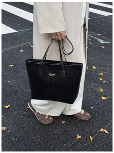 Detail of leopard print tote bag with gold lettering and black handles in autumn street setting