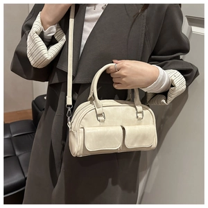 Close-up of cream Boston bag with dual front pockets and silver buckles on brown coat