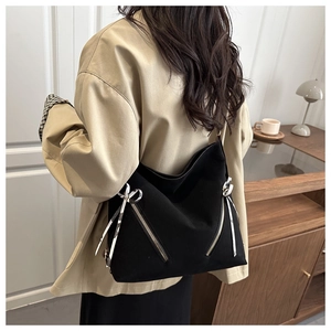 Detail of black canvas tote bag showing side metal zipper and checkered bow ribbon decoration