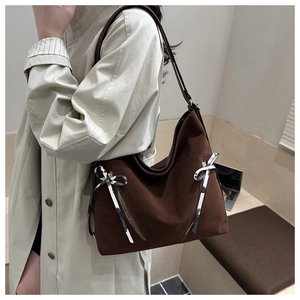 Detail of dark brown suede tote bag with metal zippers and decorative bow ribbons