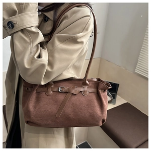 Detail of brown suede tote bag with metal buckle strap shown on a model's shoulder