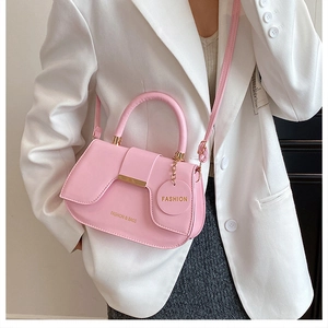 Sacoche selle rose pâle avec détails dorés et bandoulière portée sur un blazer blanc