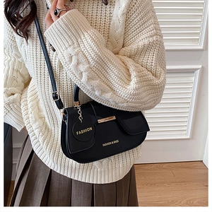 Détail du sac bandoulière noir avec barre dorée et étiquette Fashion sur un pull en maille