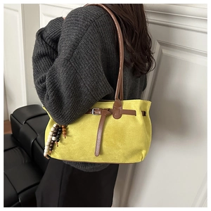 Detail of yellow suede tote bag with brown leather straps and colorful bead tassels
