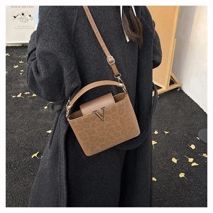 Vue détaillée du sac seau léopard marron avec fermoir en V doré sur un manteau noir élégant