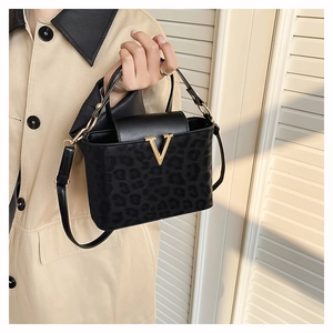 Détail du sac bandoulière léopard noir avec boucle V dorée porté sur un trench beige