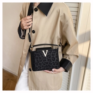 Detail of leopard print crossbody bag with gold V-buckle and black leather handles