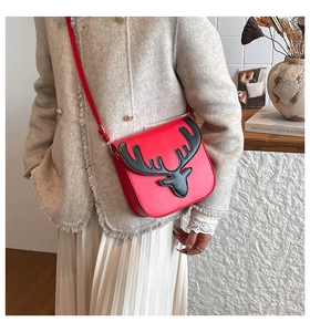 Détail du sac bandoulière rouge avec bois de renne sur fond d'étagère en bois