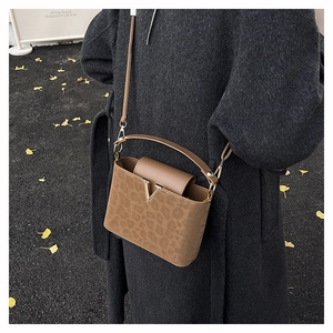 Détail du sac boîte en daim marron avec logo V doré et texture léopard en automne