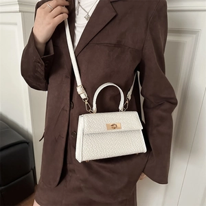 Petit sac à main blanc motif crocodile avec fermoir doré porté sur un blazer brun