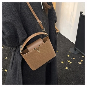 Detail of suede crossbody box bag featuring leopard print base and gold V-shaped buckle