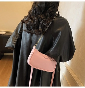 Pink litchi texture crescent bag with gold chain strap on black leather coat