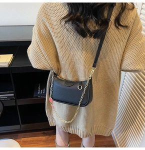 Détail du sac demi-lune en cuir grainé noir avec chaîne dorée sur un pull en maille