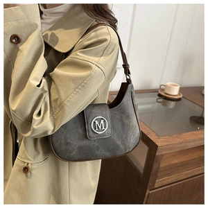 Détail du sac demi-lune en daim gris avec bordure marron et logo M sur un trench-coat