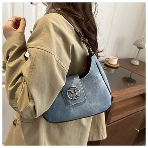 Detail of blue denim crescent bag featuring brown leather trim and metallic M logo buckle