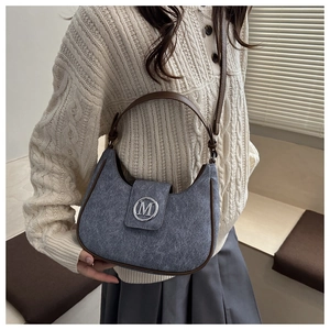 Detail of blue denim hobo bag featuring brown leather trim and silver M-logo buckle