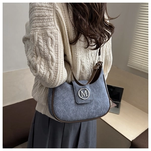 Detail view of a grey shoulder bag with silver M logo and brown leather strap on model