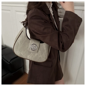 Detail of a half-moon shoulder bag in sage suede with brown leather trim and M-buckle