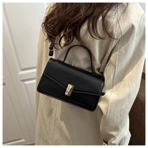 Detail of a black leather crossbody bag with gold buckle on a beige trench coat