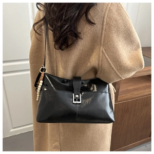 Détail du sac à main noir brillant avec perles en bois porté sur un manteau de laine