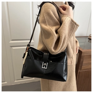 Close-up of black glossy shoulder bag with silver buckle and beaded charm detail