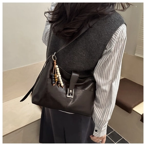 Detail of a dark brown vintage leather crossbody bag with a colorful beaded tassel pendant