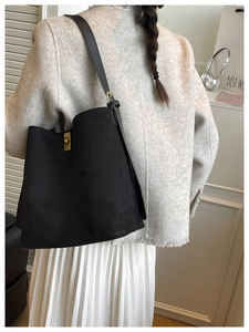 Close-up of black suede bucket bag with brown leather strap and gold buckle detail