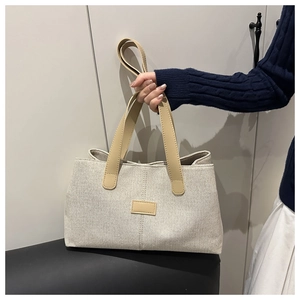 Détail du sac cabas en toile avec anses brunes tenu par un mannequin en pull bleu marine