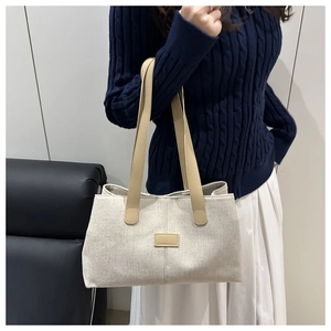 Close-up of cream canvas tote bag with brown leather straps shown on a model