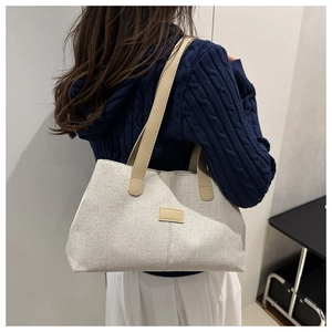 Detail of grey canvas tote bag with brown leather handles and a minimalist aesthetic