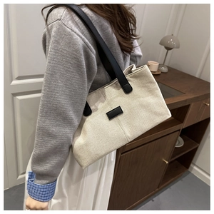 Détail d'un sac cabas en toile beige minimaliste avec bandoulières en cuir noir et écusson