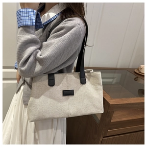 Detail of off-white canvas tote bag with black leather strap and rectangular logo patch