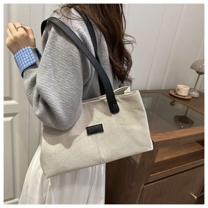 Détail d'un sac cabas en toile minimaliste avec anses en cuir noir et surpiqûres verticales