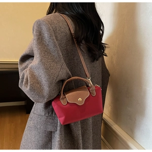 Detail of red nylon mini bag with brown leather flap and handle worn by model