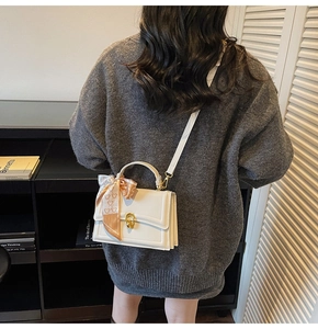 Détail d'un sac à main blanc avec fermoir doré et foulard en soie à motif ours décoratif