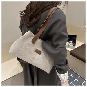Rear view of a model carrying a cream canvas tote bag with brown leather accents