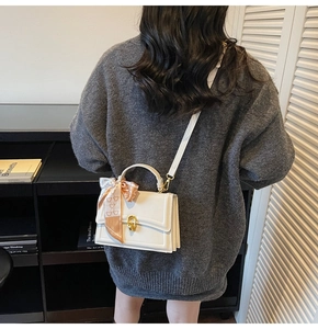 Dettaglio borsa a mano bianca con chiusura dorata e foulard in seta sul manico